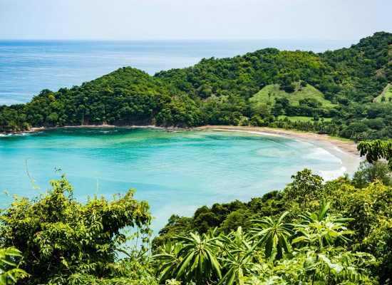 View of a small crescent beach hidden away among green hills and forests.  Punta Islita Beach, Guanacaste, Costa Rica